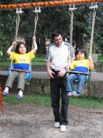 Deux enfants sur une balançoire sont aidés par un adulte.
