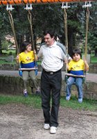 Deux enfants sur une balançoire sont aidés par un adulte.
