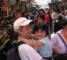 Un enfant dans les bras d'une femme, au milieu de monde dans une rue piétonne bordée de magasins.