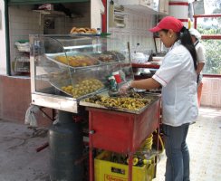 Une femme se tient debout devant un étalage de produits cuisinés.