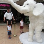 Un homme et 2 enfants se tiennent auprès d'une statue d'éléphant.