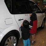 Deux enfants dessinent sur une voiture blanche.