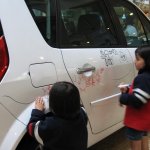 Deux enfants dessinent sur une voiture blanche.