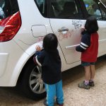 Deux enfants dessinent sur une voiture blanche.