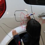 Un enfant dessine sur une voiture blanche.