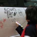 Un enfant dessine sur une voiture blanche.