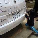 Un enfant dessine sur une voiture blanche.