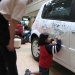 Un enfant écrit son prénom sur une voiture blanche.