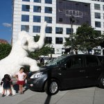 Un éléphant en statue et 2 enfants devant une voiture.