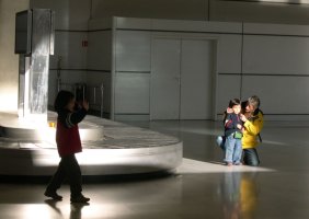 A l'aéroport, un enfant marche et un autre se tient debout à côté d'une femme agenouillée.