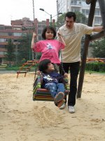 Deux enfants sur une balançoire, poussée par un homme.