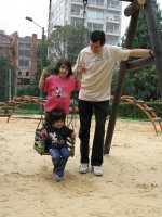 Deux enfants sur une balançoire, poussée par un homme.