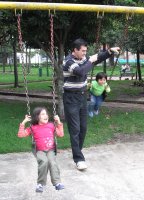 Deux enfants sont chacun sur une balançoire. L'un des enfants est aidé par un homme.
