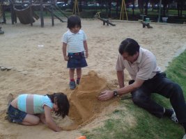 Deux enfants et une homme jouent dans le sable.