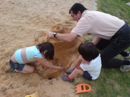 Deux enfants et une homme jouent dans le sable.
