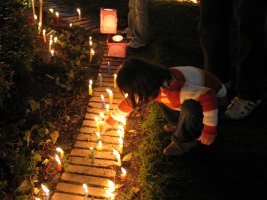 Un enfant se tient accroupi auprès de bougies allumées sur le sol.