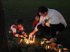 Un homme et deux enfants se tiennent accroupis auprès de bougies allumées sur le sol.
