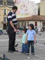 Un homme et deux enfants sur une place avec des pigeons.