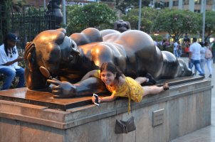 Une femme allongée à côté d'une statue de Botero représentant une femme allongée sur le ventre.