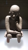 Statue en pierre d'une personne ayant les coudes sur les genoux.
