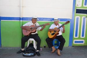 2 hommes jouent de la guitare, assis sur un tabouret.