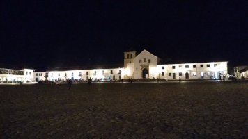 Grande place du village bordée d'un bâtiment illuminé, le soir.