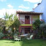 Extérieur de maison avec son petit jardin. Une table ronde et 4 chaises sont disposées dans l'herbe.