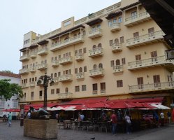 Immeuble avec balcons. Au pied de l'immeuble, less parasols rouges d'un restaurant.