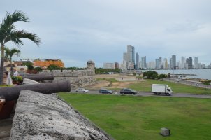 Au 1er plan, 2 canons posés sur le contrefort. Au fond, les gratte-ciels. Devant, grande plaine avec 2 rues qui se croisent. Le tout, en bord de mer.