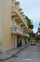 Rue avec la façade de maisons de couleur jaune pastel. Un taxi jaune passe dans la rue.