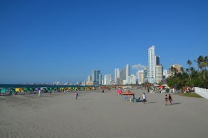 Gratte-ciels en bord de plage, plage avec des parasols de toutes les couleurs et quelques promeneurs.