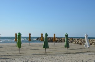 Parasols verts, oranges et blanc, fermés, plantés sur le sable.