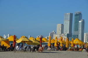 Gratte-ciels au fond et parasols jaune-orange sur la plage.