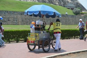 Homme à côté de son vélo cargo contenant de la boisson et un parasol.