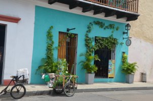 Façade bleu-vert d'une maison avec un chariot et un vélo garés au bord du trottoir.
