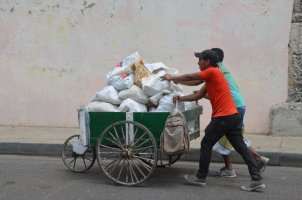 2 hommes poussent un chariot à 3 roues contenant des sacs pleins.