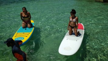 Carole et Paola en paddle, à genou, dans une eau claire, le formateur à leur côté.